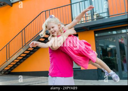 Heureuse mère balançant et filant fille mignonne en cercles par les bras à l'extérieur. Gamin ludique énergique et joyeux s'amusant tout en se liant à maman Banque D'Images