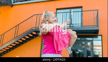 Heureuse mère balançant et filant fille mignonne en cercles par les bras à l'extérieur. Gamin ludique énergique et joyeux s'amusant tout en se liant à maman Banque D'Images