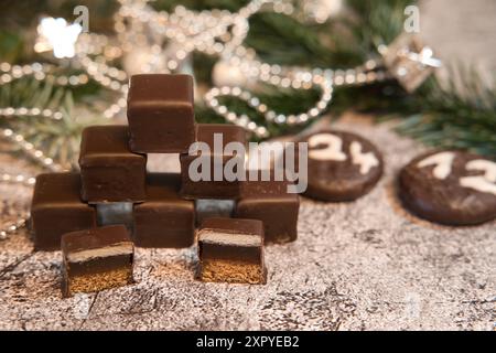 Dominos empilés devant des sapins et une chaîne de Noël avec des biscuits ronds au chocolat portant la date du réveillon de Noël Banque D'Images