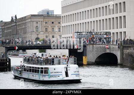 Berlin, Allemagne. 08 août 2024. Un bateau d'excursion navigue sur la Spree devant un pont au Forum Humboldt, sur lequel circule un bus pour les visites de la ville. Crédit : Sebastian Gollnow/dpa/Alamy Live News Banque D'Images