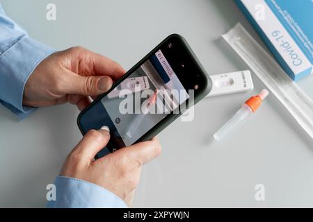 Mains féminines faisant une photo du kit d'auto-test avec un résultat positif covid 19 avec une caméra phoner à envoyer à un médecin. Kit de support d'auto-test Banque D'Images