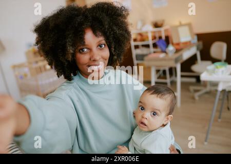 Maman blogueuse afro-américaine prenant selfie avec son petit garçon dans la crèche Banque D'Images