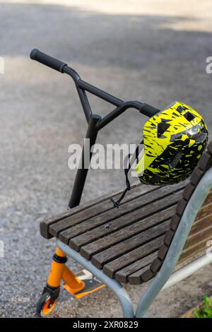 Casque et scooter sportif pour enfants dans le parc près du banc. Banque D'Images
