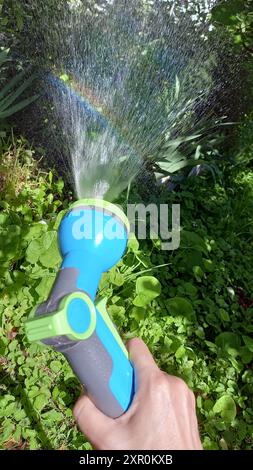 Tuyau d'arrosage dans la main de la femme, arroser le jardin potager. Reflets de l'arc-en-ciel. Gros plan. Banque D'Images