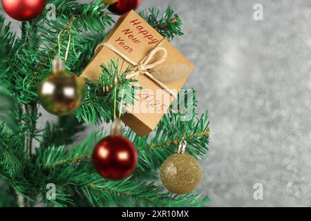 Coffret cadeau avec bonne année et 2025 écrit en rouge sur le dessus de l'arbre de Noël décoré de boules rouges et dorées devant un fond gris. Banque D'Images