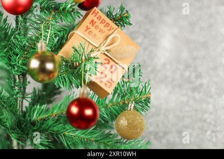 Coffret cadeau avec bonne année et 2025 écrit en rouge sur le dessus de l'arbre de Noël décoré de boules rouges et dorées devant un fond gris. Banque D'Images