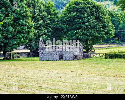 Chalet en pierre en ruine entouré d'arbres verdoyants dans un cadre de campagne serein Banque D'Images