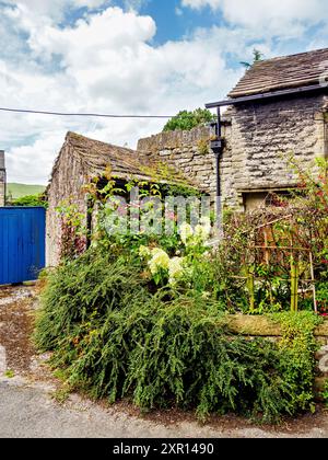 Charmant cottage en pierre avec une végétation luxuriante et des fleurs en fleurs, situé sous un ciel partiellement nuageux. Banque D'Images