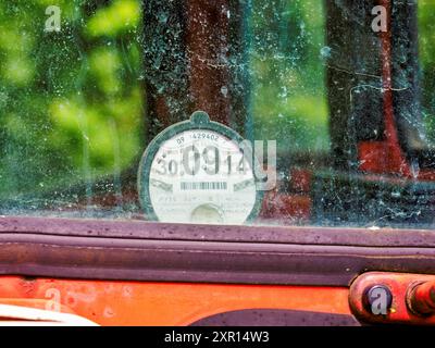 Gros plan du disque de taxe routière expiré d'un véhicule d'époque derrière un pare-brise poussiéreux. Banque D'Images