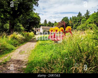 Chemin rural menant à une ferme en pierre, entouré de verdure luxuriante et d'équipements agricoles. Banque D'Images