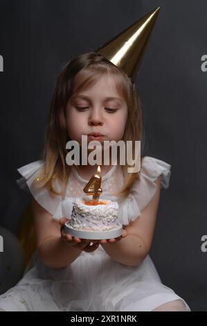 Une petite fille d'anniversaire avec un gâteau. souffle les bougies. vertical Banque D'Images