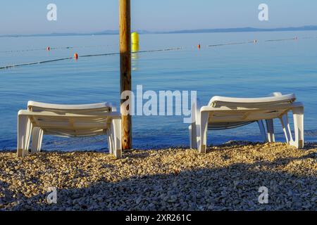 Chaises longues sur la plage sous parasols de paille au bord de la mer Banque D'Images