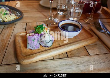Rouleau vietnamien avec des légumes coupés en morceaux avec un bol blanc avec de la sauce soja sur un plateau en bois sur la table dans un restaurant ou à la maison Banque D'Images
