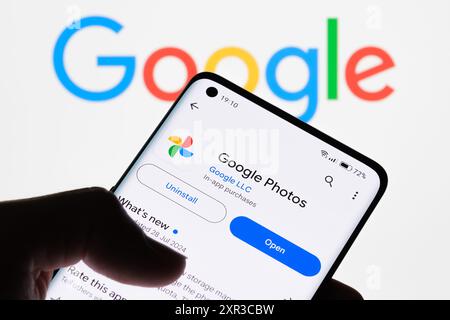 Gros plan de l'écran d'un smartphone affichant l'application Google photos avec le logo Google en arrière-plan, démontrant la connexion entre Google photos et Banque D'Images