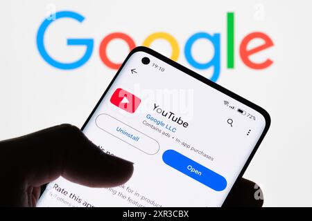 Gros plan de l'écran d'un smartphone affichant l'application YouTube avec le logo Google en arrière-plan, illustrant la connexion entre YouTube et Google, Sta Banque D'Images