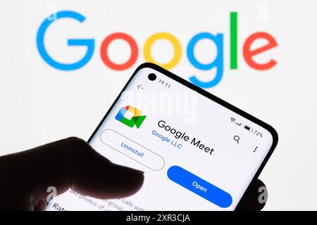 Gros plan de l'écran d'un smartphone affichant l'application Google Meet avec le logo Google en arrière-plan, mettant en évidence la connexion entre Google Meet et Goo Banque D'Images