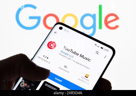 Gros plan de l'écran d'un smartphone affichant l'application YouTube Music avec le logo Google en arrière-plan, illustrant la connexion entre YouTube Music et Banque D'Images