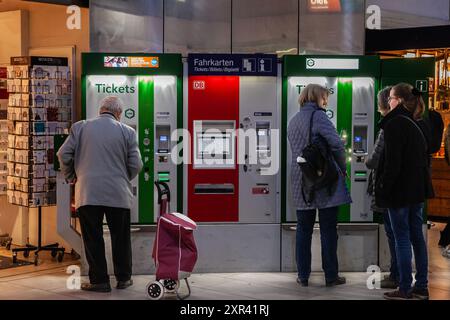 Une image représentant des passagers à la gare de Dusseldorf Hbf en Allemagne, utilisant des distributeurs automatiques pour acheter des billets de train. La photo reflète le hus Banque D'Images