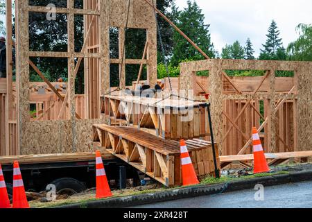 Construction de maisons résidentielles, grue à flèche soulevant la livraison de bois, poutres de treillis de soutien en bois chaînées à la grue et levage de début Banque D'Images