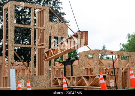 Construction de maisons résidentielles, grue à flèche soulevant la livraison de bois, poutres de treillis de soutien en bois chaînées à la grue et levage de début Banque D'Images