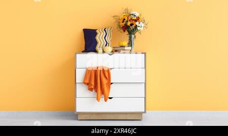 Commode blanche avec bouquet de fleurs d'automne et de citrouilles près du mur jaune Banque D'Images