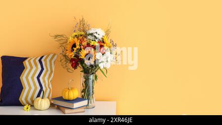 Commode avec bouquet de fleurs d'automne, livres et citrouilles près du mur jaune. Bannière pour la conception Banque D'Images