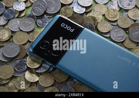 Terengganu, Malaisie - 24 août 2024 : gros plan de xiaomi poco m5 bleu sur des pièces de monnaie malaisiennes dispersées Banque D'Images