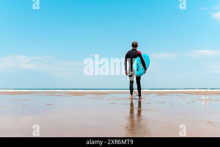 surfez sur la plage avec la planche à la main regardant l'horizon et se préparant à surfer Banque D'Images