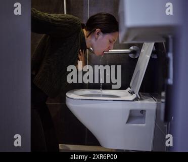 Salle de bain, vomi et femme avec douleur, plancher et symptômes d'intoxication alimentaire, malade et fatigué de la maladie. Maison, toilettes et maux de tête de personne au sol Banque D'Images