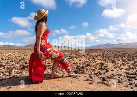 Femme avec valise rouge sur une route déserte dans le paysage aride Banque D'Images