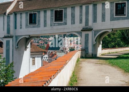 Une vue panoramique capture une arche menant à un sentier sinueux, offrant un aperçu d'un charmant village. Des maisons pittoresques parsèment le paysage, encadrées par lu Banque D'Images