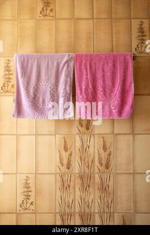 Serviettes fraîches aux couleurs vives suspendues à un cintre de salle de bain en métal, placées contre un mur de carreaux vintage. Banque D'Images