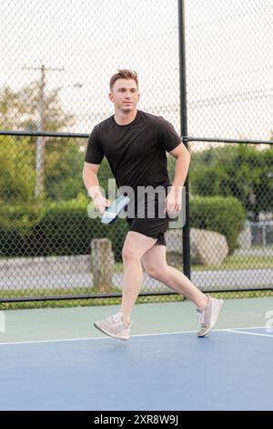 Jeune homme en action jouant au pickleball sur un terrain extérieur. Banque D'Images