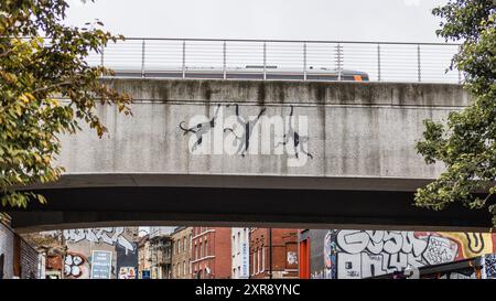 Série animalière londonienne de Banksy : trois singes oscillants sur un pont ferroviaire sur Brick Lane à Shoreditch alors qu'un train passe. Banque D'Images