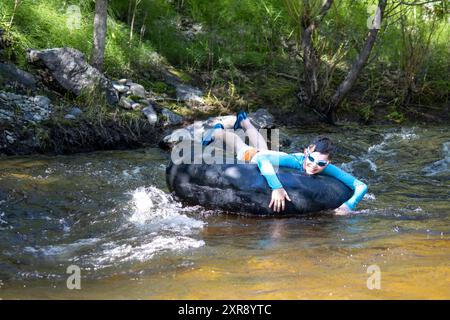 Garçon profitant du tube dans un ruisseau, portant des lunettes de protection et une protection anti-éruption Banque D'Images