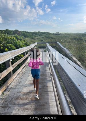 Jeune fille courant sur une promenade en bois à travers la verdure luxuriante t Banque D'Images