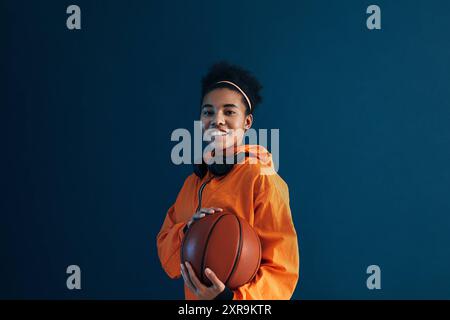 Femme souriante avec basket portant des vêtements de sport orange et regardant la caméra. Joueur professionnel de basket-ball posant en studio. Femme souriante avec b Banque D'Images