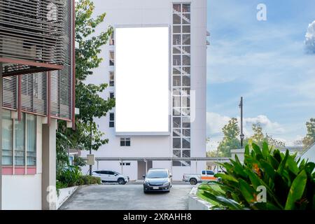 Un grand panneau d'affichage vierge se dresse sur le côté d'un grand bâtiment moderne. Le panneau d'affichage est blanc avec un fond blanc, chemin de détourage. Les voitures sont garées Banque D'Images