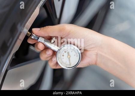 Une personne vérifie la pression des pneus d'une voiture à l'aide d'un manomètre. La personne tient le manomètre d'une main et appuie dessus Banque D'Images