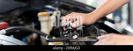 Une personne tient un entonnoir et verse du liquide de refroidissement dans le radiateur d'une voiture et ils se tiennent devant une voiture. Le capot de la voiture est ouvert, et Banque D'Images