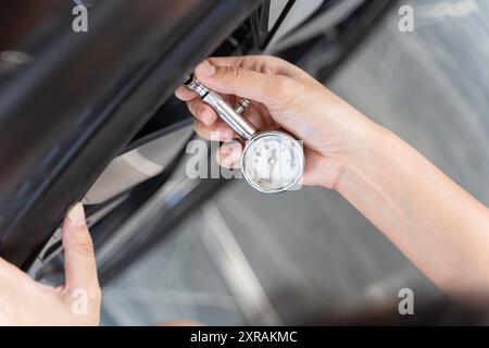 Gros plan du manomètre tenant la main pour mesurer la pression des pneus de voiture. Fille Vérifiez les pneus avant de partir. Fille vérifiant l'état de la voiture. Femme vérifiant Banque D'Images