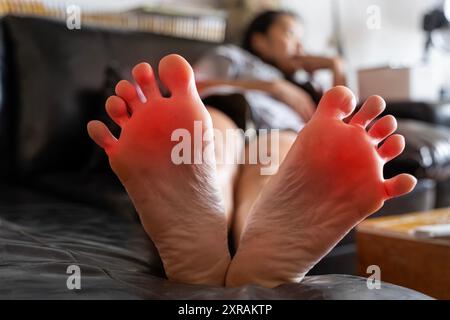 Douleur dans le pied, fille tient ses mains à ses pieds, massage des pieds, crampes, spasme musculaire, accent rouge sur le pied, photo noir et blanc, gros plan. Healthca Banque D'Images