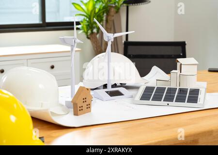 Éoliennes et cellules solaires Un chapeau d'ingénieur blanc et jaune est assis sur la table. Concept d'énergie renouvelable. Panneaux solaires et éolienne portable sur Banque D'Images