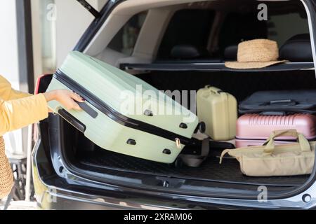 Femme chargeant la valise dans le coffre de voiture, préparation pour le voyage. Coffre de voiture ouvert emballé pour des vacances en famille. Jeune belle femme concept de voyage féminin ta Banque D'Images