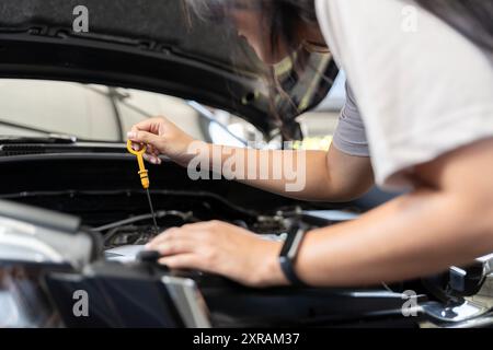 Une femme sort la jauge pour vérifier le niveau d'huile de sa voiture, photo en gros plan de la main de la femme vérifier l'huile moteur. Travailler avec la voiture dans le service de réparation Banque D'Images