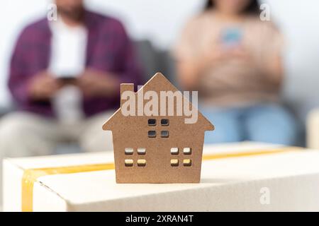 Un jeune couple utilise un smartphone pour trouver des informations sur le déménagement. Homme et femme et modèle de maison. Plan de maison sur la boîte en carton le jour du déménagement, c Banque D'Images