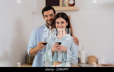Couple heureux tenant des verres à vin touchant les fronts profitant d'un moment tendre, date romantique debout dans la cuisine moderne à la maison ensemble, femme souriante Banque D'Images
