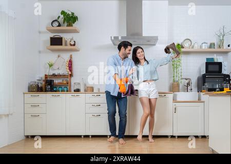 Concept de nettoyage. Joyeuse jeune femme européenne et masculine lavant la vaisselle dans l'intérieur de la cuisine moderne. Hygiène, tâches ménagères dans le temps libre. Jeune fami Banque D'Images