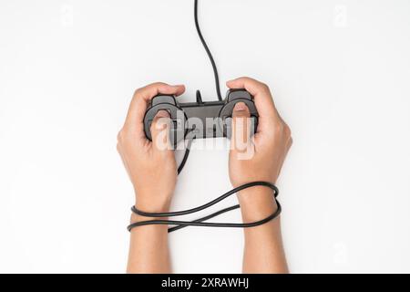 Addiction aux jeux vidéo. Fil et manette de jeu ou joystick, mains câblées avec joypad signifiant addiction au jeu vidéo. Banque D'Images