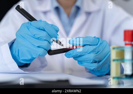 Femme travaillant avec un échantillon de sang dans le laboratoire. La main du docteur tenant un flacon d'échantillon de sang, un dispositif médical de test sanguin, tenant un flacon de sang sam Banque D'Images